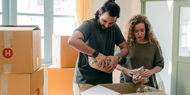 diverse-couple-packing-belongings-in-parchment-near-different-boxes-indoors